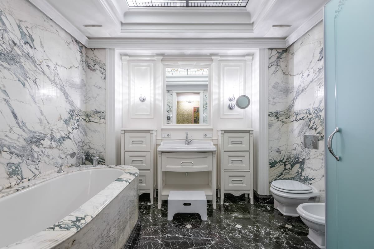 Bathroom with veined marble walls, an oval tub, a white paneled vanity and a dark marble floor