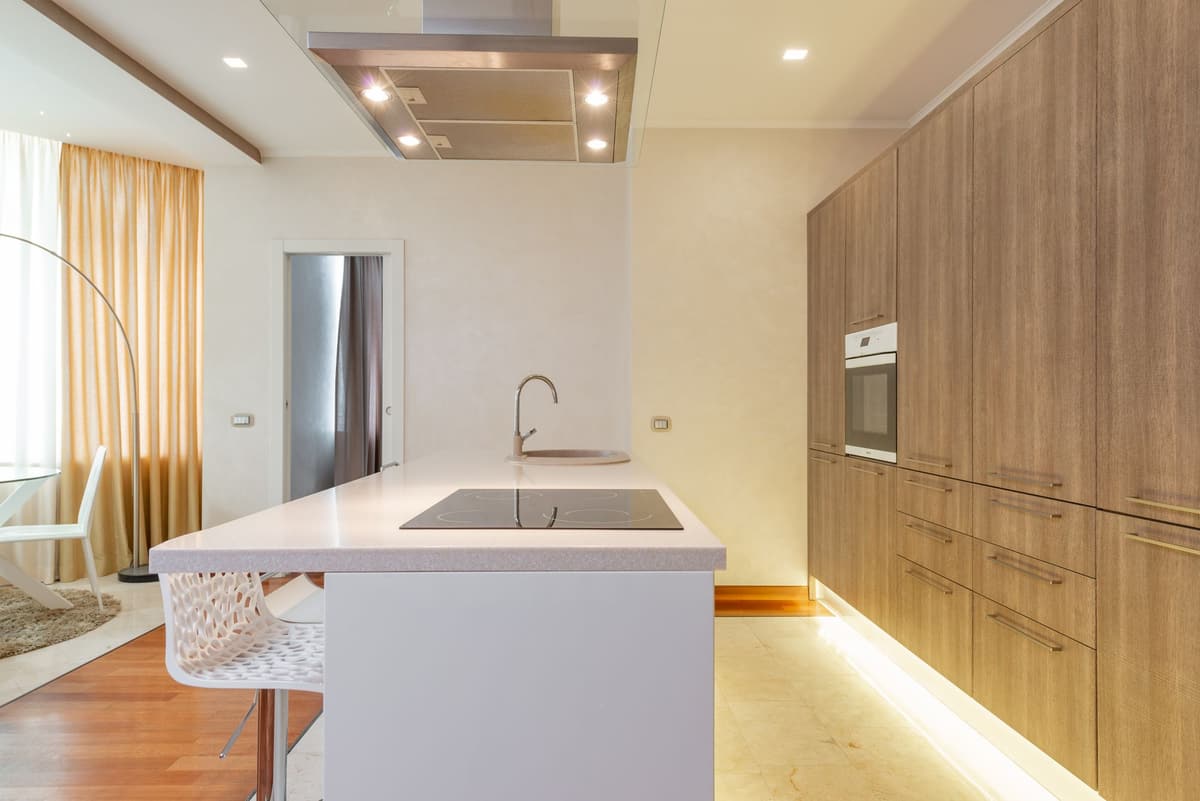 Kitchen with tall wood-grain cabinetry, a white island with a cooktop and a softly lit toe-kick